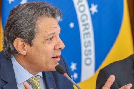 O ministro da Fazenda, Fernando Haddad, em reunião com o presidente Lula e lideranças políticas no Planalto. Ele gesticula enquanto fala diante de microfone - Metrópoles