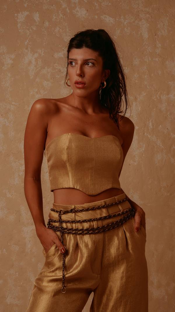 Modelo branca, alta e magra usa top estilo corset metalizado, cinto de corrente e calça dourada - Metrópoles