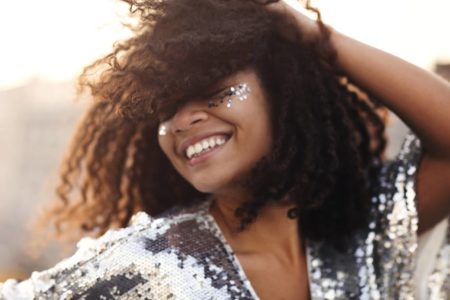 Mulher negra e de cabelo cacheado com maquiagem de glitter e roupa de paetê