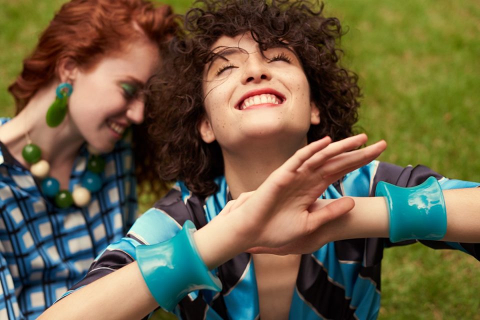 Duas mulheres brancas em jovens posam para foto em um jardim na campanha da marca Abi Project. A primeira modelo possui os cabelos cacheados castanhos e a segunda é ruiva. - Metrópoles