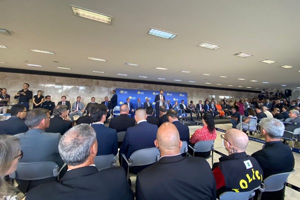 Fotografia colorida de plateia em frente a grupo de pessoas em palco