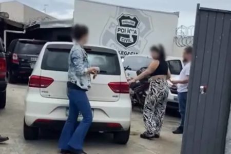 Imamgem mostra mulheres próximas a um carro branco em uma delegacia. Uma jovem teria tentado matar o ex-marido e o amigo por ciúmes - Metrópoles