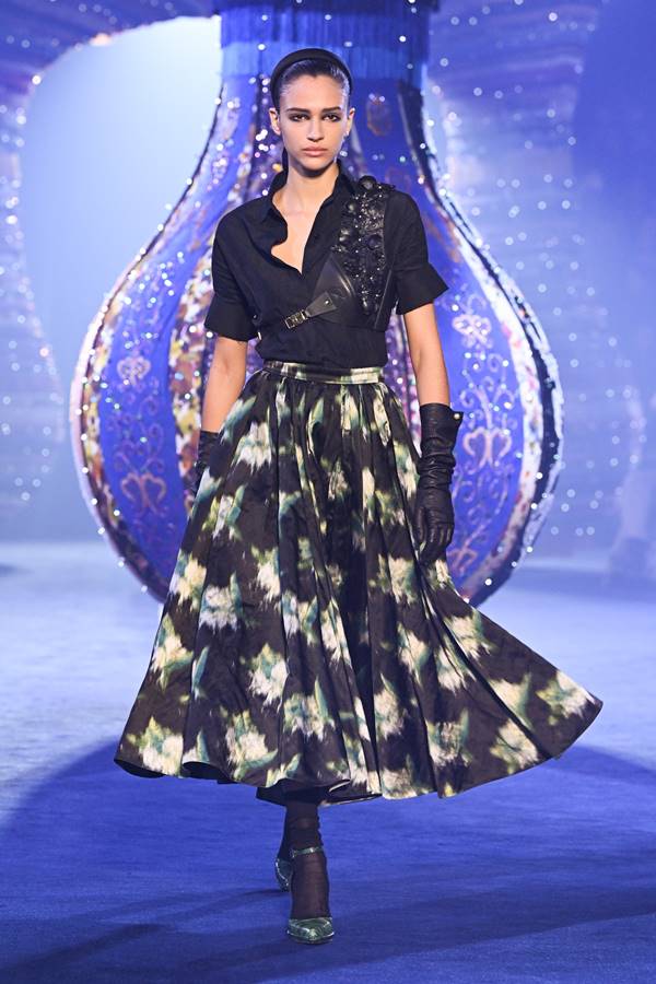Modelo da Dior usa saia midi florida, camisa preta, pochete, luvas e sandálias de salto alto com meias - Metrópoles