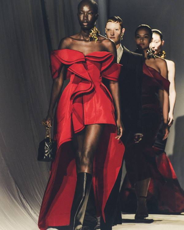 Modelos na passarela da marca Alexander McQueen. Modelo da frente é negra e usa vestido vermelho com babados e assimetrias - Metrópoles
