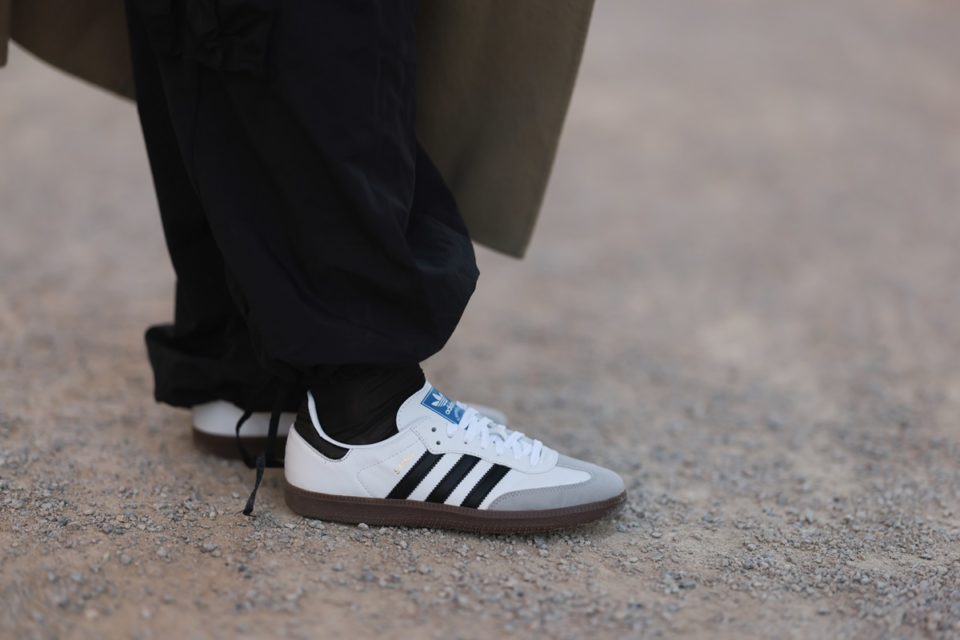 Pessoa na Semana de Moda de Paris. Ela usa uma calça preta, meia preta e o tênis esportivo Samba, da marca Adidas, na cor branca com as listras pretas. - Metrópoles