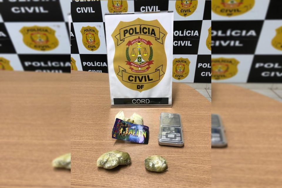 Pacotes de drogas dispostos em mesa de madeira com placa mostrando o símbolo da PCDF