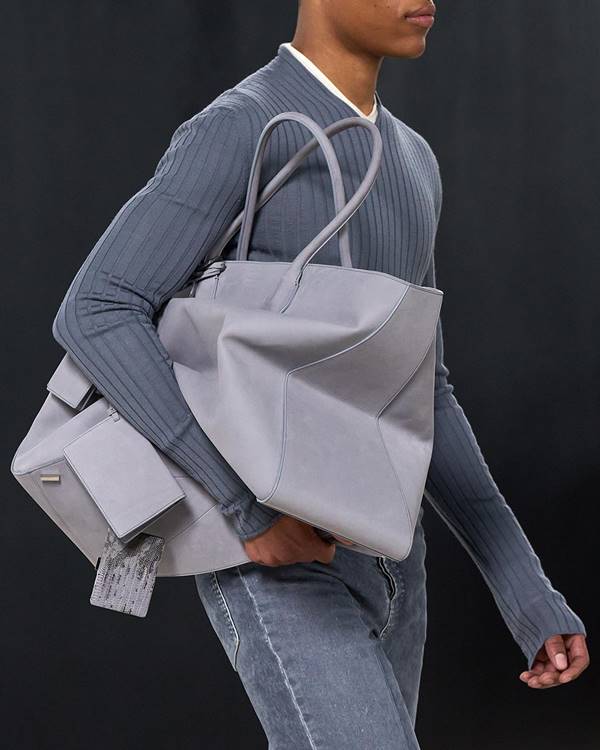 Modelo usa suéter cinza e usa bolsa grande cinza debaixo do braço - Metrópoles
