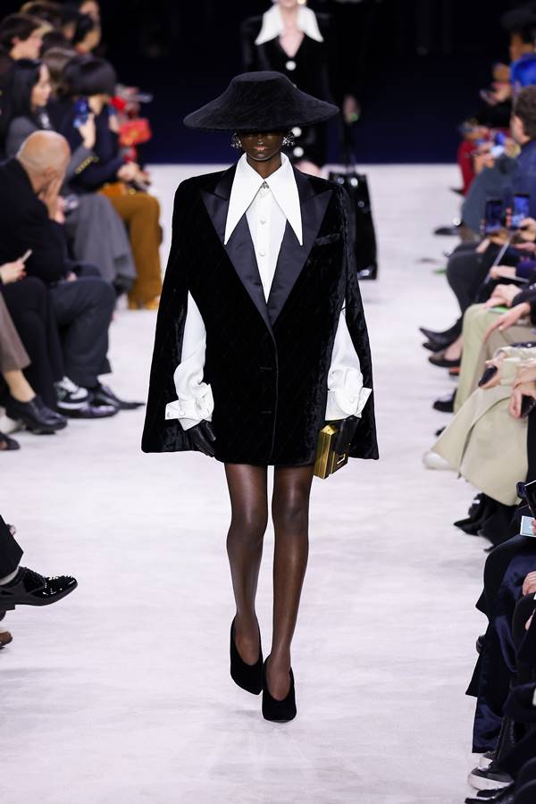 Modelo negra na passarela de moda usa camisa branca com gola pontuda, casaco morcego e saltos altos - Metrópoles