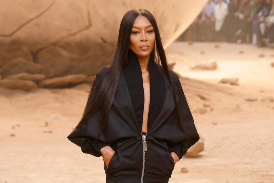 Naomi Campbell em passarela de moda com vestido preto decotado - Metrópoles