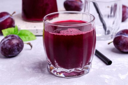 Copo de suco de ameixa com ameixas em volta