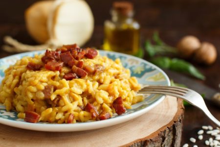 Risoto de bacon servido em um prato fundo com detalhes azul e um garfo - metrópoles