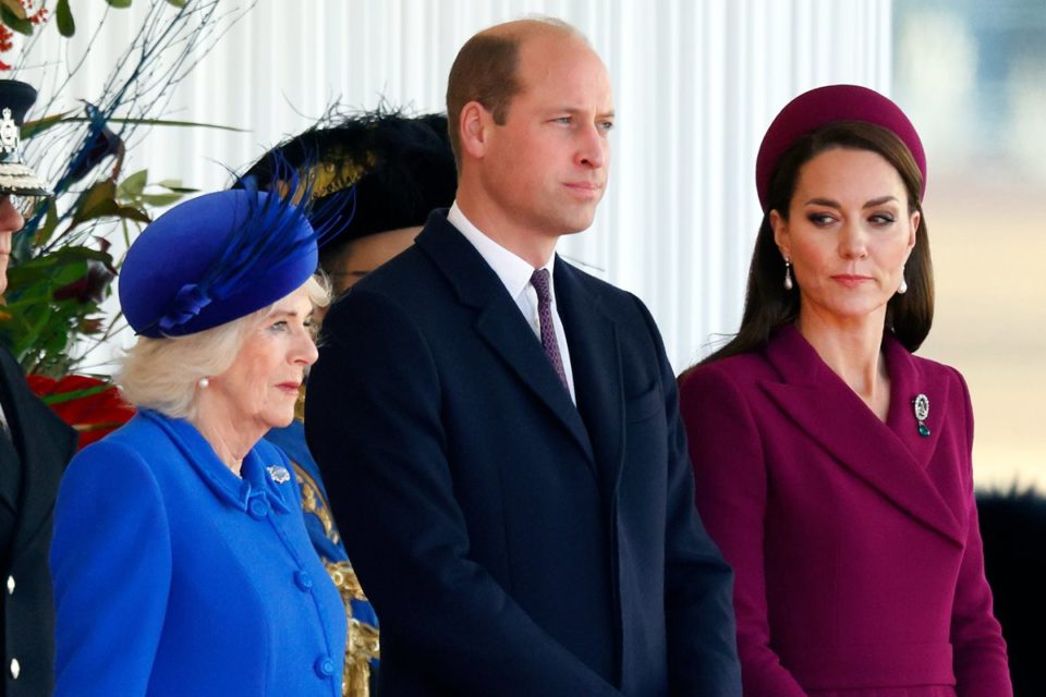 Foto colorida de mulher branca, idosa e com roupa azul ao lado de homem branco, careca e vestido com terno e de mulher branca, com cabelo castanho e roupa fúcsia - Metrópoles