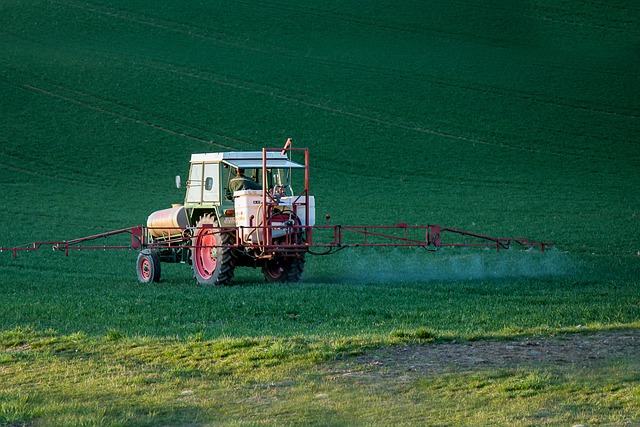 Imagem colorida de trator espalhando agrotóxico sobre um campo verde