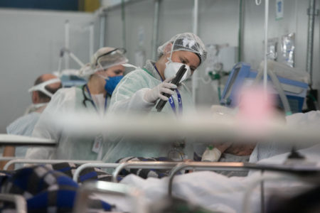 Imagem de médicos atendendo em galpão com pacientes deitados sobre macas em hospital de campanha improvisado para tratamento de infectados com Covid