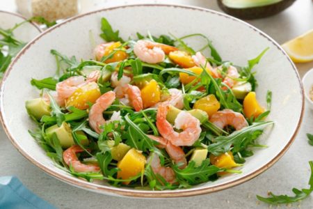 Salada tropical com camarões em prato branco com fio de ouro nas bordas em cima de uma bancada branca - Metrópoles