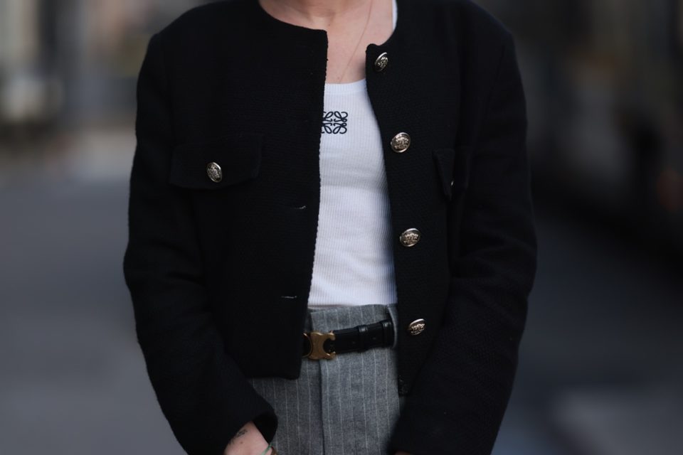 Mulher branca usa look durante a Semana de Moda de Paris. Ela veste uma regata branca com a marca da Loewe, um casaquinho preto e uma calça cinza - Metrópoles