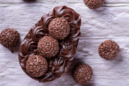 Ovo de pascoa de colher sabor brigadeiro em cima de uma bancada cinca com vários brigadeiros em volta - Metrópoles