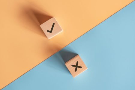 Dados com a letra x e um certo de cada lado do papel azul com laranja - Metrópoles