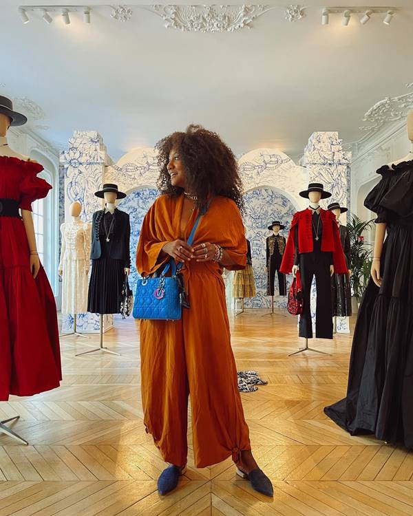 Luiza Brasil usa roupa laranja e bolsa azul e posa ao lado de manequins com roupas de grife - Metrópoles