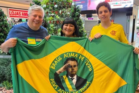 Imagem colorida mostra José Trabulo Junior, à esquerda de azul, segurando uma bandeira do Brasil com a foto de Jair Bolsonaro - Metrópoles