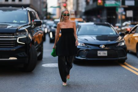 Mulher branca e jovem, de loiro liso, posa para foto andando na rua em Nova York. Ela usa um vestido curto e uma calça, tudo na cor preta. - Metrópoles