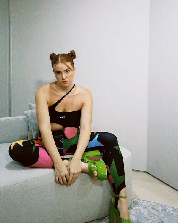 Mulher branca usa top preta, calça colorida e salto verde - Metrópoles