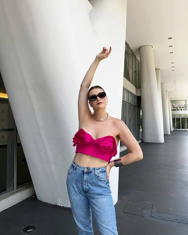 Mulher branca usa top rosa, calça jeans e cabelo preso - Metrópoles