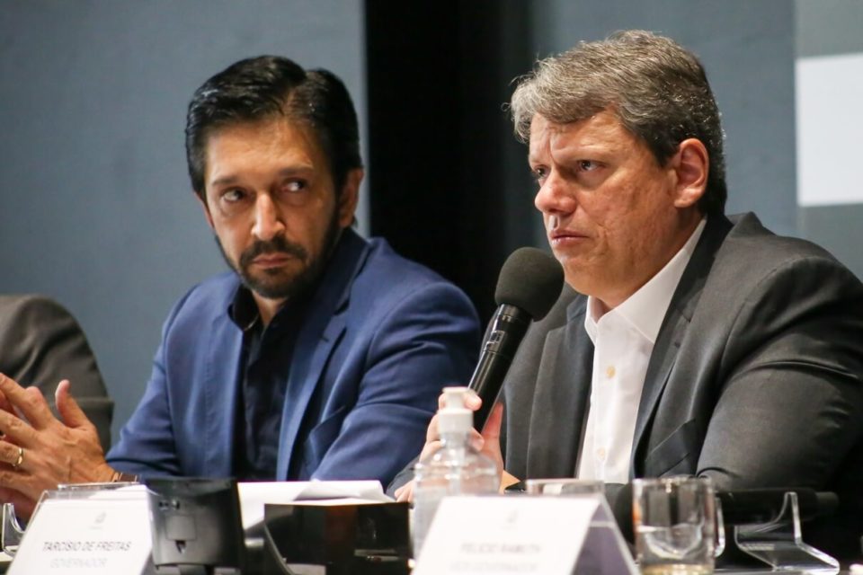 O prefeito de São Paulo, Ricardo Nunes, observa o governador de São Paulo, Tarcísio de Freitas, durante discurso em cerimônia oficial