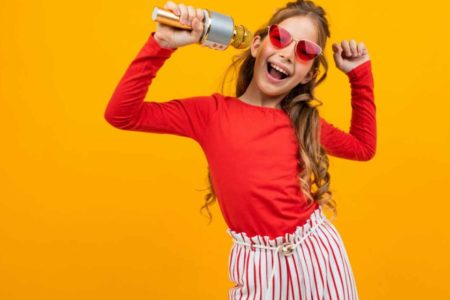 menina com blusa vermelha óculos em formato de coração cantando e sorridente - signos - Metrópoles