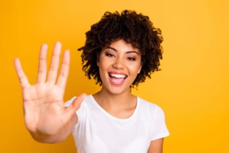 Mulher de cabelo curto fazendo o numero 5 com as mãos usando um blusa branca - Metrópoles