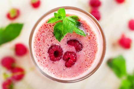Copo de smoothie de frutas vermelhas visto de cima com folhina de hortela na borda