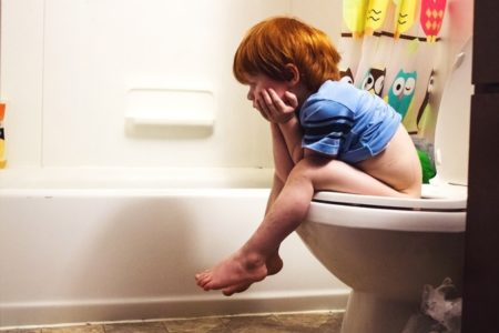 Imagem colorida: menino sentado no vaso sanitário
