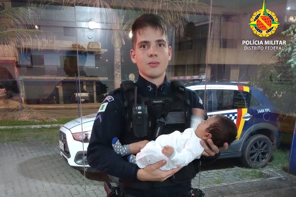 Fotografia colorida de policial militar fardado segurando bebê no colo