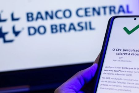 imagem colorida de uma mão segurando um celular para consultar dinheiro esquecido no Banco Central