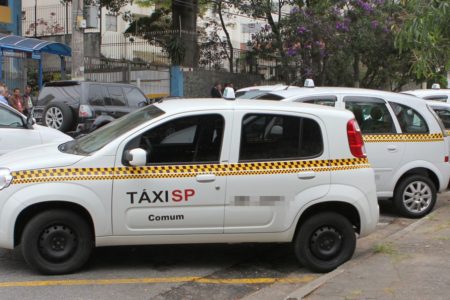 Imagem colorida com táxi da cidade de SP, um carro branco com detalhes em amarelo