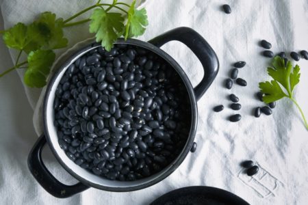 Foto de feijão preto dentro de uma panela preta, rodeada com cheiro-verde - Metrópoles