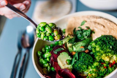 Tigela com legumes, verduras e grãos nutritivos e uma mãe segurando colher