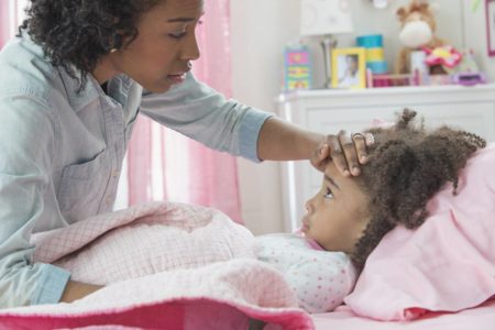 Mãe tocando testa da filha deitada na cama com lençois cor de rosa