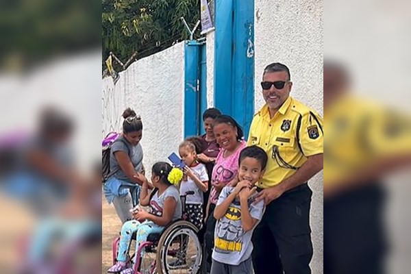 Fotografia colorida de homem de farda amarela com crianças em porta de escola