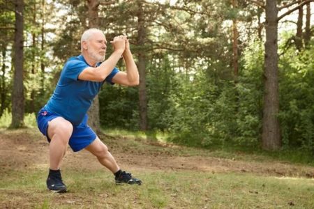 Idoso com barba vestido de azul faz exercício ao ar livre em área verde - Metrópoles