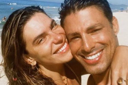 Foto colorida de Mariana Goldfarb e Cauã Reymond sorrindo em praia - Metrópoles