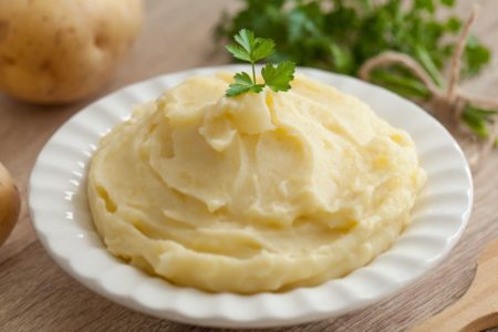 Purê de batata grosso dentro de um prato branco com salsaa por cima e ao fundo batatas grandes - metrópoles