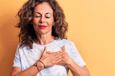 mulher com a mão no coração e de olhos fechados - metrópoles