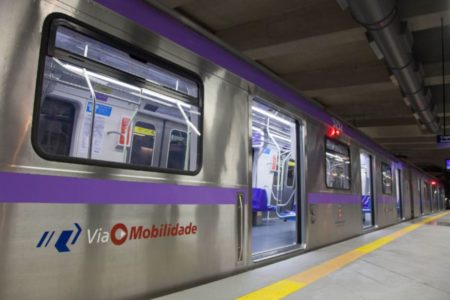 Imagem colorida mostra trem prateado, com faixa lilás, sob as janelas do metrô de São Paulo - Metrópoles