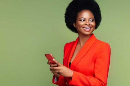 Mulher com blaser laranjado segurando um celular na mão - Metrópoles