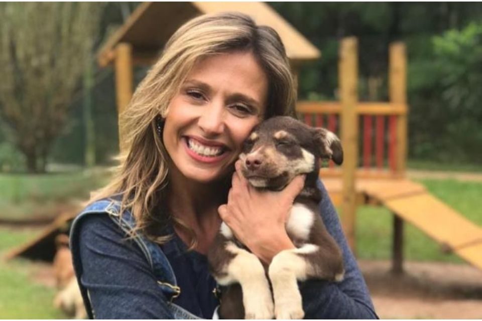 Foto colorida de uma mulher branca, loira, segurando um cachorro no colo - Metrópoles