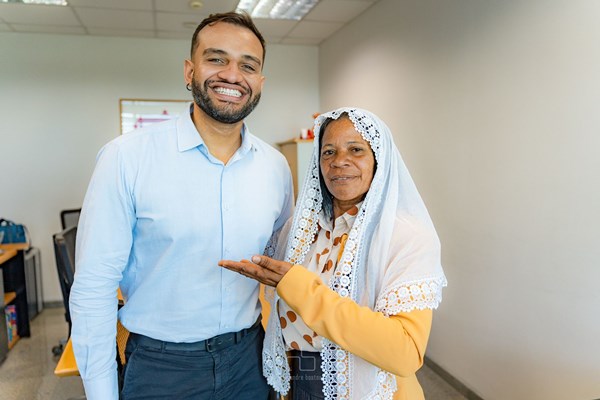 Fotografia colorida mostra homem de camisa azul sorrindo ao lado de mulher de véu branco