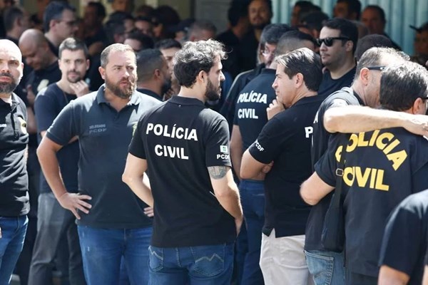 Fotografia colorida mostra homens de preto com uniforme da Polícia Civil