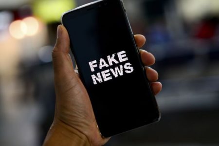 Pessoa segura celular com uma tela escrito "fake news" - Metrópoles