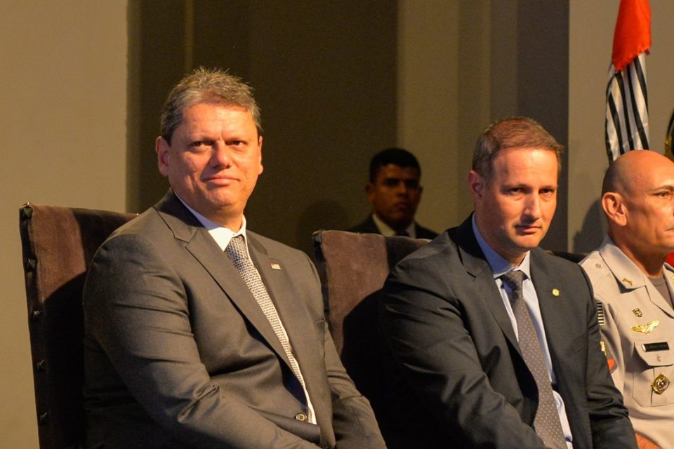 PCC Imagem colorida do governador de São Paulo Tarcísio de Freitas sentado ao lado do secretário de Segurança Pública Guilherme Derrite. Os dois estão vestidos de terno e gravata
